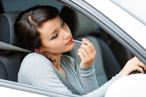 A young woman applying makeup in the car while driving