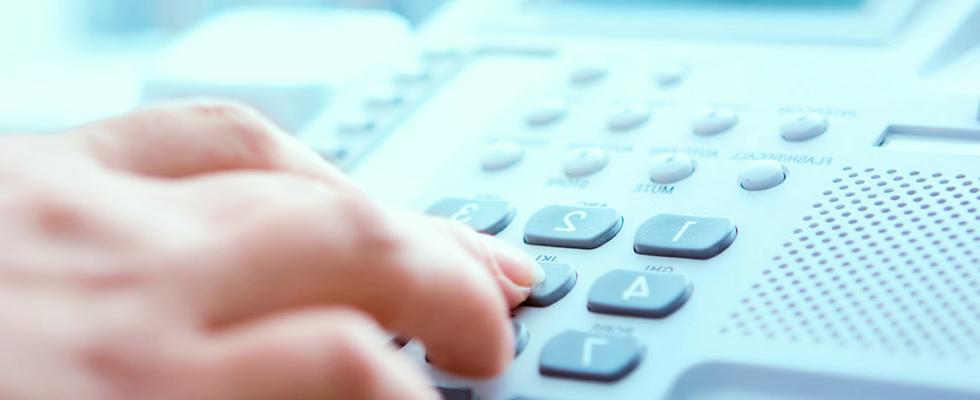 Closeup photo of a hand dialing a desk phone